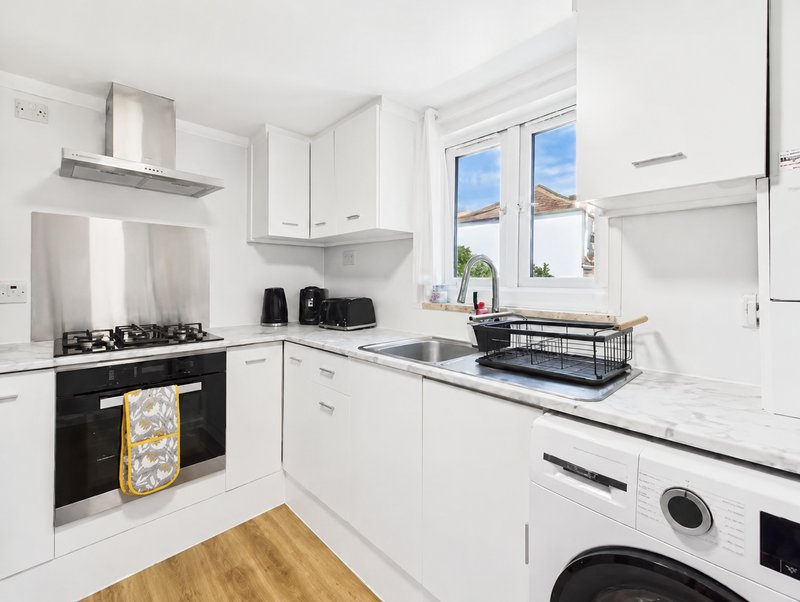 Modern white kitchen with gas hob, dishwasher, washing machine and natural light from window