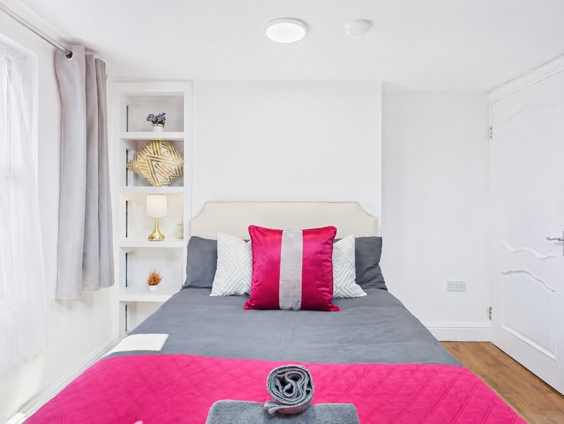 Modern bedroom with double bed, pink and grey cushions, built-in shelving, and wooden floor