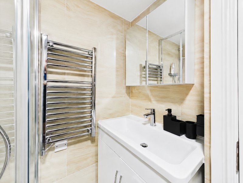 Modern bathroom with heated towel rail, white vanity, mirror and cream tile walls