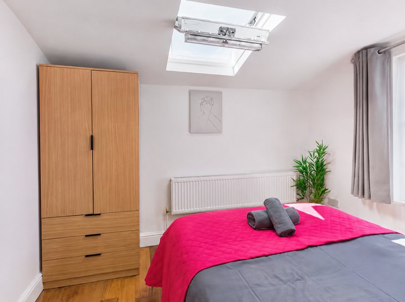 Bright bedroom with double bed, pink bedding, wooden wardrobe, radiator and skylight window
