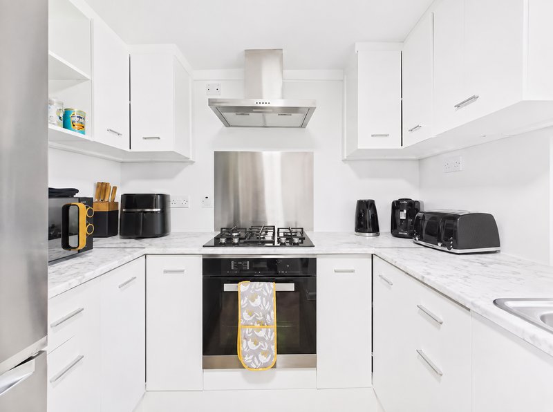 Modern white kitchen with gas range, stainless steel extractor hood, and black appliances