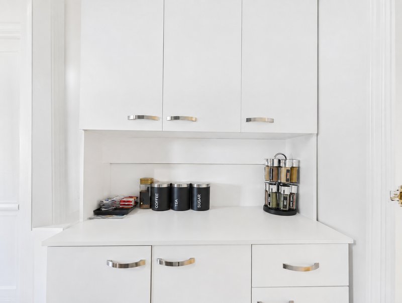 White kitchen cabinet with open shelving displaying black canisters and kitchen accessories