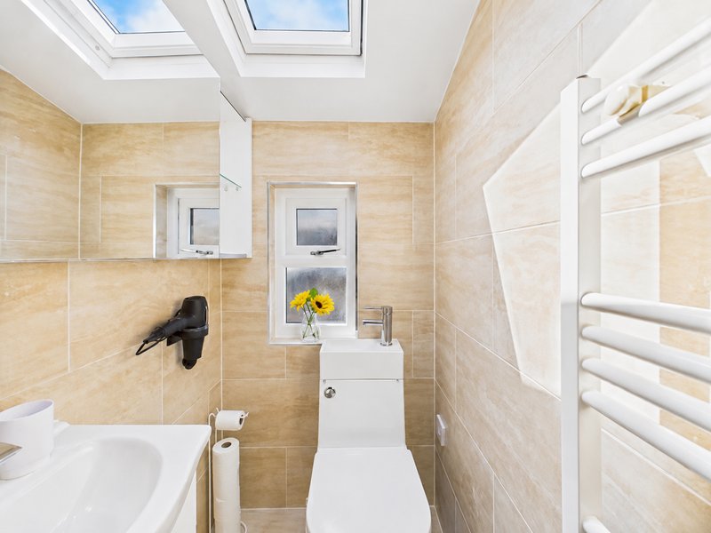 Modern bathroom with beige tile walls, white toilet, sink, heated towel rail and skylight