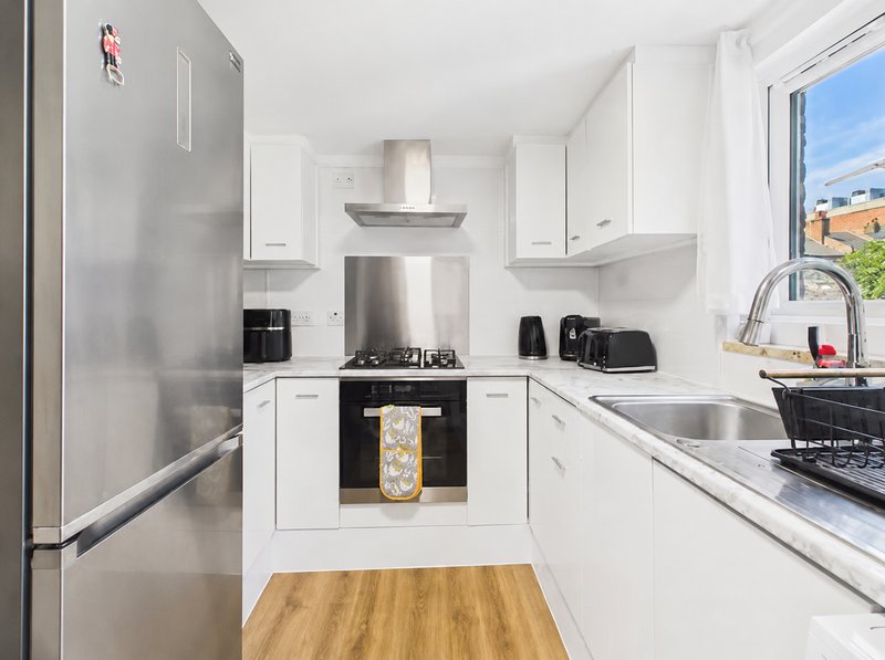 Modern kitchen with white cabinets, stainless steel appliances, wooden flooring and window