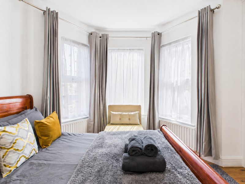 Bright bedroom with double bed, bay windows, grey curtains and rolled towels