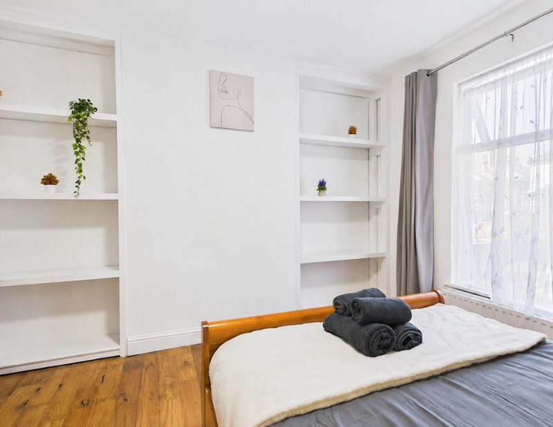 Bright bedroom with wooden bed frame, white shelving, hardwood flooring and large window