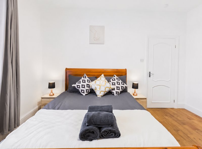 Bedroom with double bed, wooden headboard, patterned pillows, and rolled towels on bed