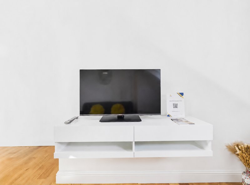 White TV stand with flat-screen television, wooden flooring, and minimal decor