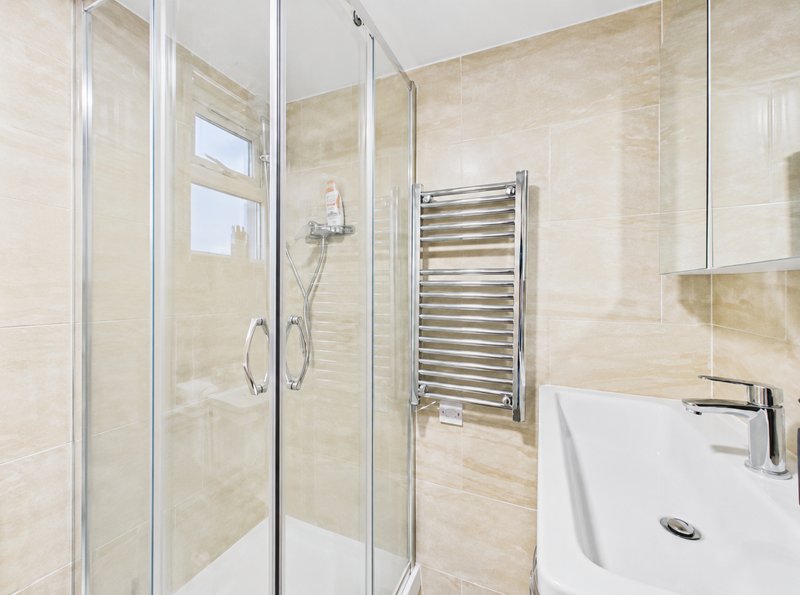 Modern bathroom with walk-in shower, heated towel rack, white sink and beige tiles