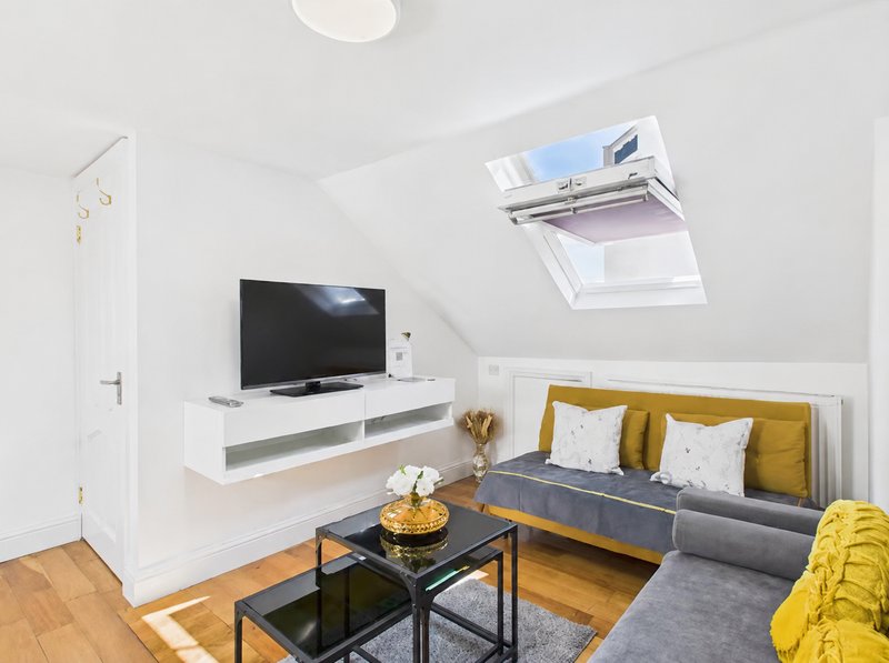 Modern attic studio with yellow and gray sofa, wall-mounted TV, skylight and wooden flooring