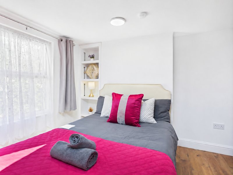 Modern bedroom with double bed, pink and grey bedding, built-in shelving, and large window with curtains
