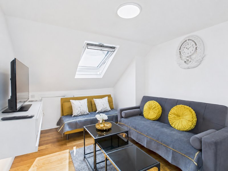 Modern attic living room with grey sofa, yellow cushions, skylight window and wooden flooring