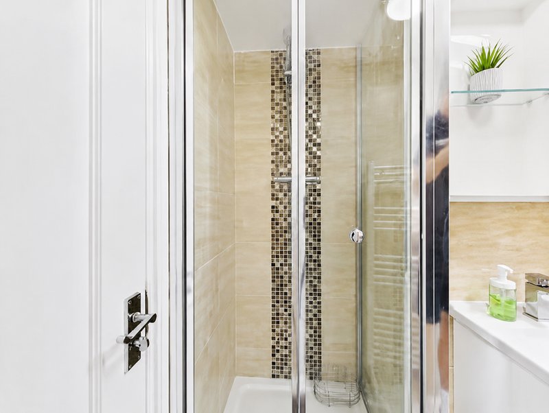 Modern bathroom with glass shower enclosure, beige tile walls, and white vanity sink