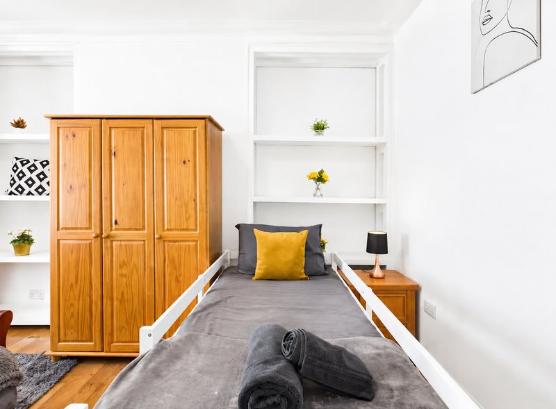 Bedroom with single bed, wooden wardrobe, white shelving, and hardwood flooring