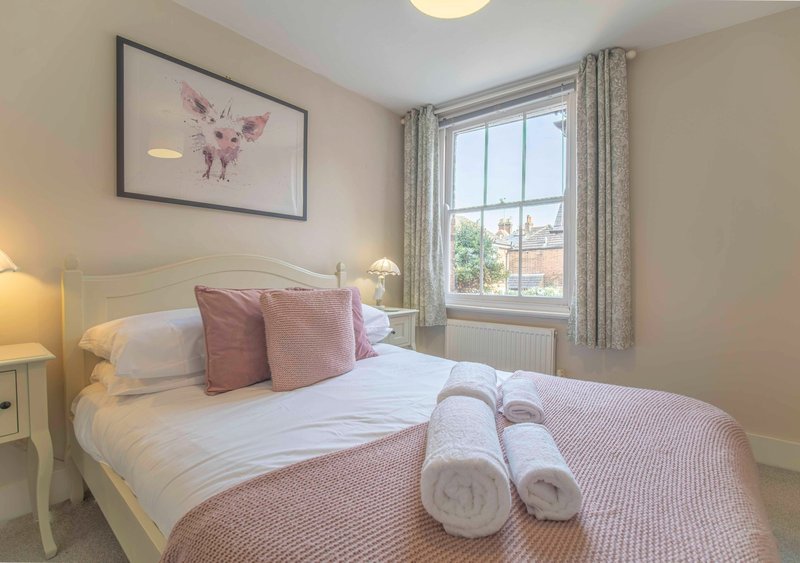 Bedroom with double bed, pink cushions, rolled towels, framed wall art and window with curtains