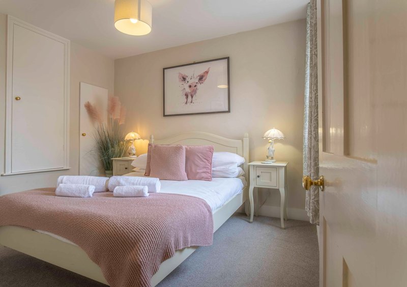 Bedroom with double bed, pink bedding, white nightstands, table lamps and framed wall art