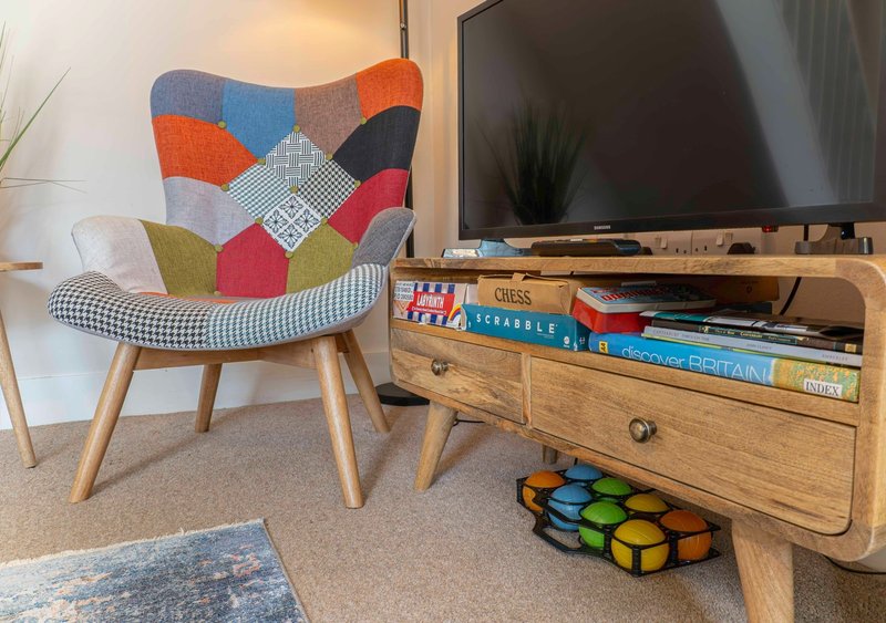 Living room with colorful patchwork armchair, wooden TV unit, wall-mounted television, and board games