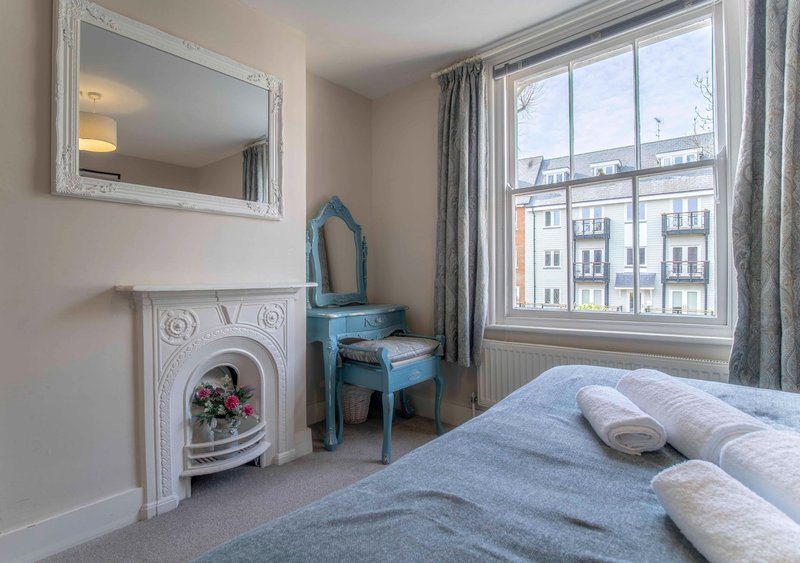Bright bedroom with double bed, fireplace, blue dresser, wall mirror and city views through large window