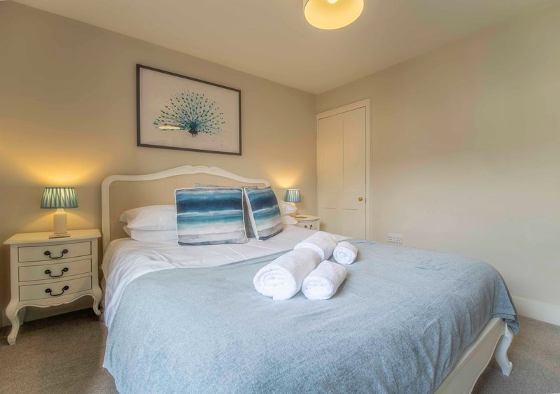 Bright bedroom with double bed, blue striped pillows, white rolled towels, bedside tables with lamps and framed wall art