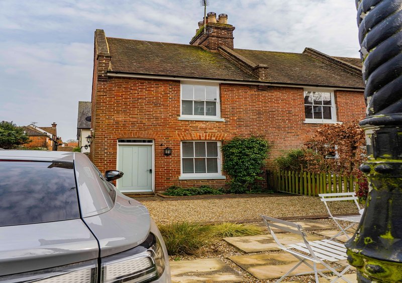 Red brick cottage with driveway, parked car, front garden and ivy-covered fence