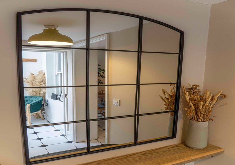 Modern arched mirror with black frame above wooden shelf, dried flowers in vase