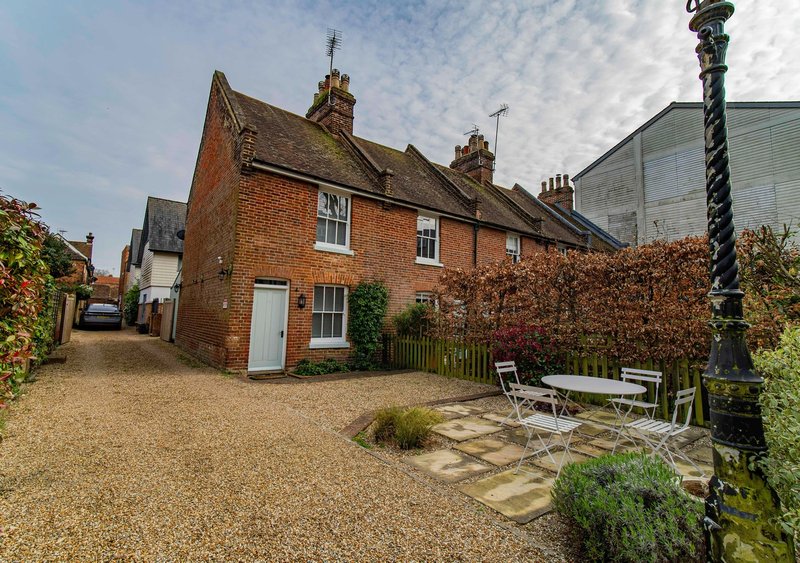 Brick cottage with driveway, patio seating area, and ivy-covered garden wall