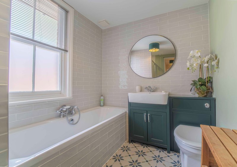 Modern bathroom with bathtub, round mirror, dark green vanity and patterned floor tiles