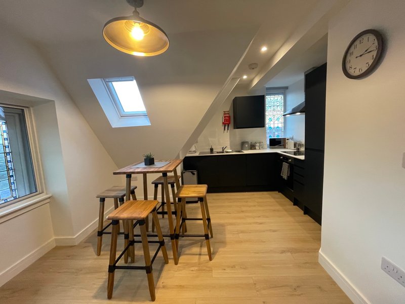 Open-plan kitchen and dining area with wooden table, bar seating, skylight and wall clock