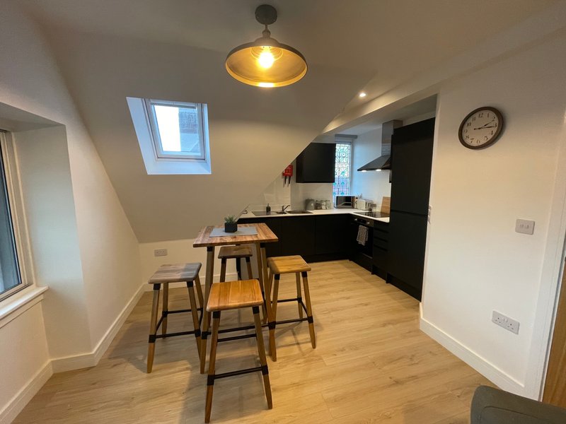 Modern kitchen and dining area with black cabinetry, wooden bar stools, and pendant lighting