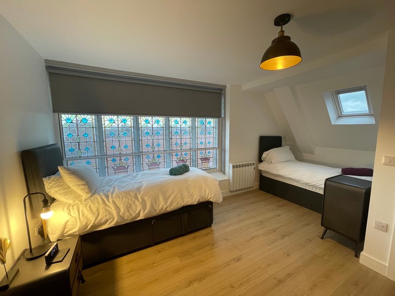 Bright attic bedroom with two single beds, wooden floor, large window and pendant lamp