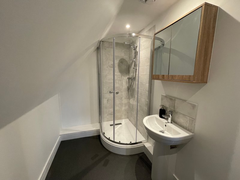 Modern bathroom with curved glass shower enclosure, white sink, mirror cabinet and dark floor