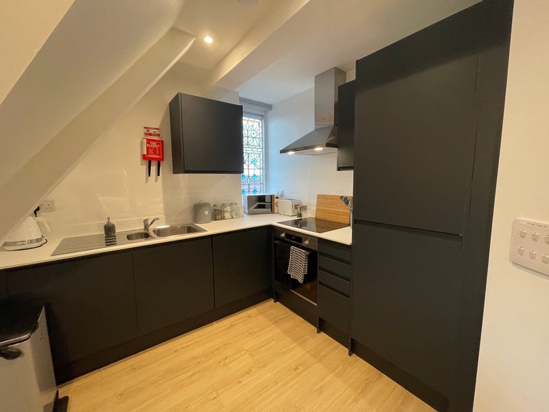 Modern kitchen with black cabinetry, wooden floor, stainless steel appliances and window