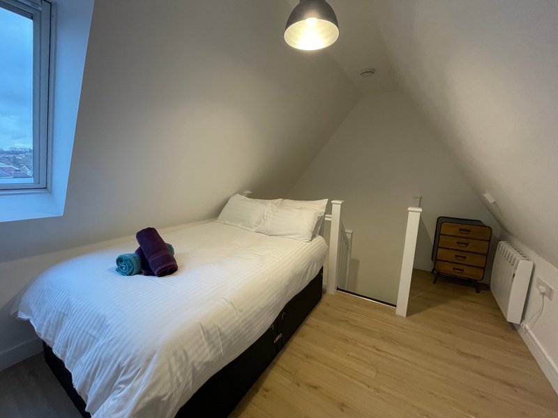 Bright attic bedroom with double bed, wooden floor, pendant light, and skylight window