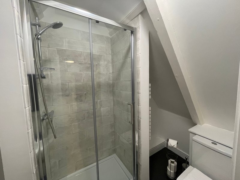 Modern bathroom with glass shower enclosure, grey tile walls, and white toilet