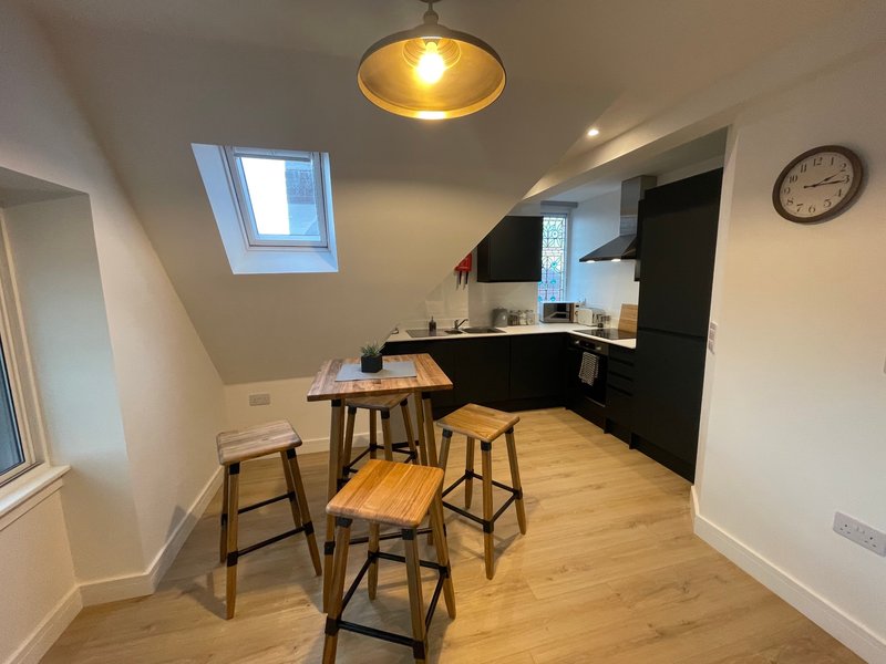 Modern kitchen with black cabinetry, wooden bar stools, dining table, and skylight window