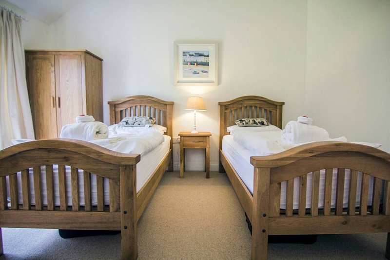 Twin bedroom with two wooden beds, bedside table, lamp, and framed artwork on wall