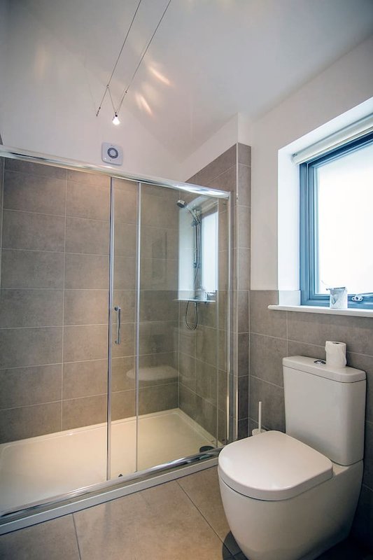 Modern bathroom with grey tile walls, walk-in shower enclosure, toilet and window