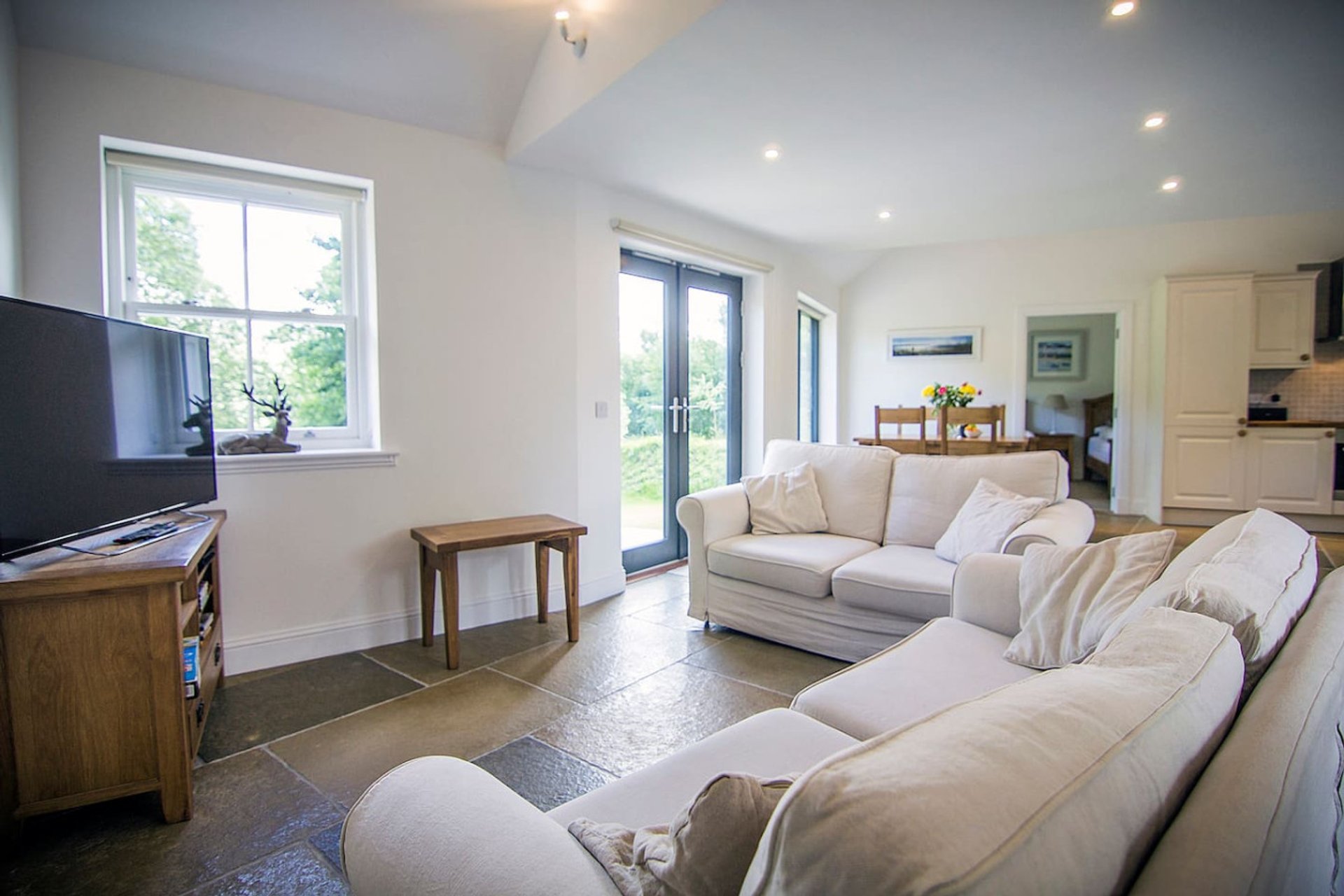 Bright open-plan living room with cream sofas, TV, wooden furniture and garden views