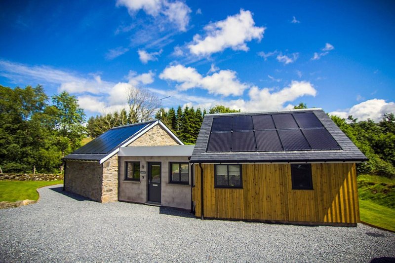 Modern single-storey property with stone and timber cladding, solar panels, surrounded by trees and garden