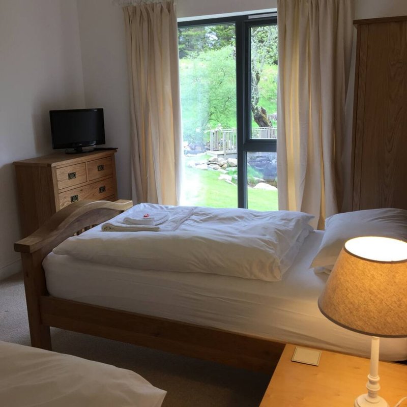 Bright bedroom with double bed, wooden furniture, TV, lamp and garden view through patio doors