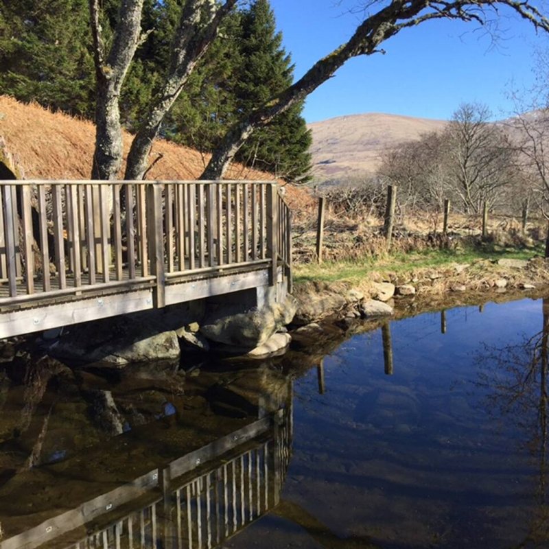 Wooden deck and railing overlooking a stream with trees and hills in background