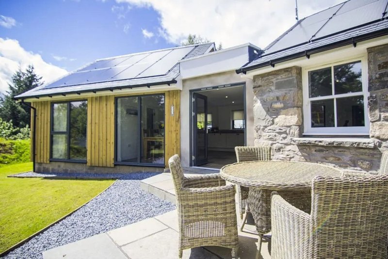 Modern stone house extension with patio, wicker seating and manicured garden