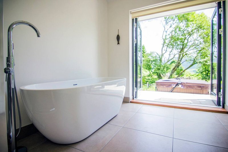 Modern bathroom with freestanding white bathtub, floor-mounted faucet, and large window overlooking garden