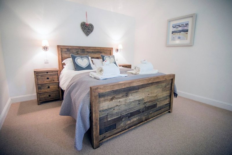 Bedroom with wooden bed frame, blue bedding, matching nightstand, heart decoration and framed picture