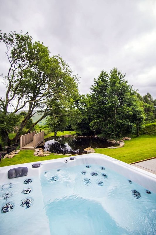 Hot tub with jets in garden overlooking lawn, trees and wooden fence