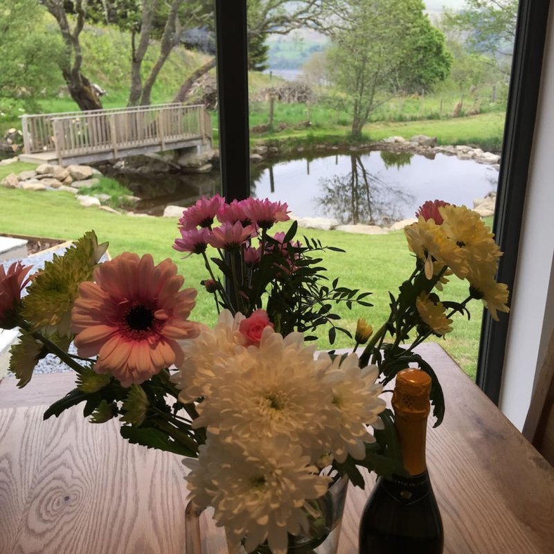 Floral arrangement on table with garden and pond visible through large windows