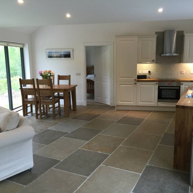 Open-plan kitchen and dining area with cream cabinetry, slate flooring, wooden table and chairs