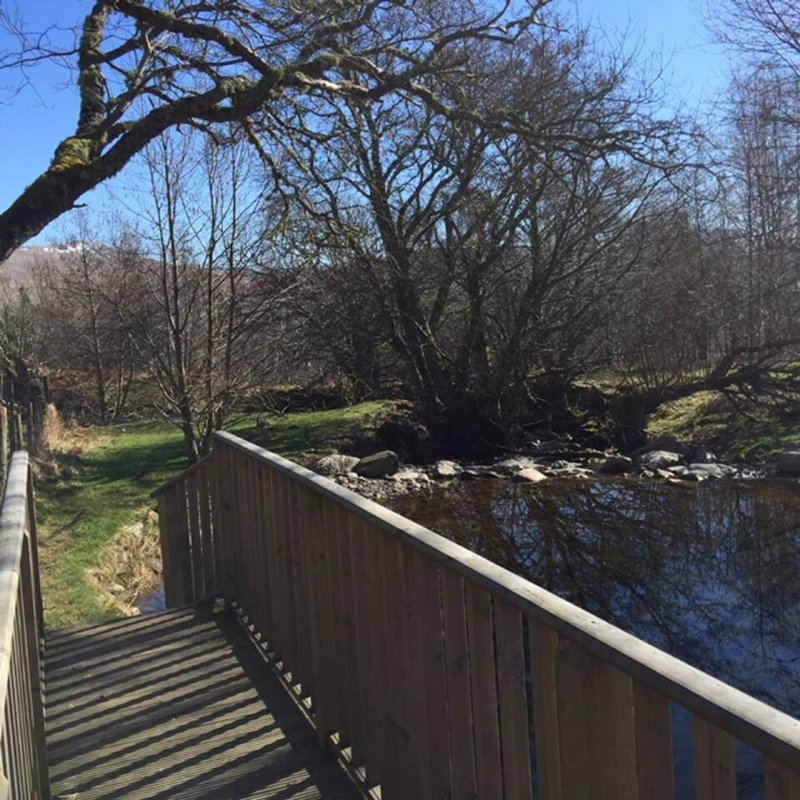 Wooden deck overlooking stream with bare trees and grassy grounds beyond