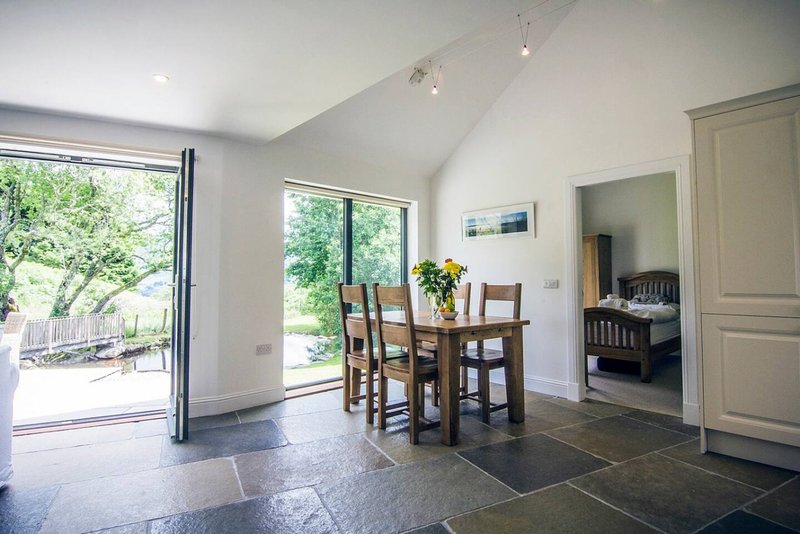Open-plan dining area with wooden table, chairs, slate flooring and garden access