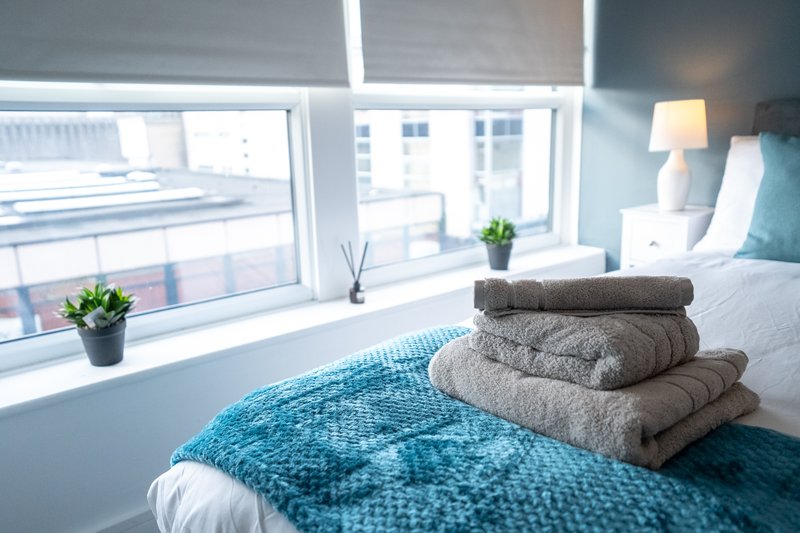 Bright bedroom with blue bedding, folded towels, potted plants and large windows
